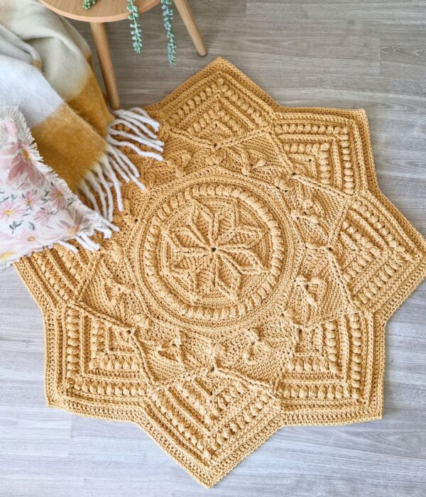 Crochet floor rug next to a table and blanket.