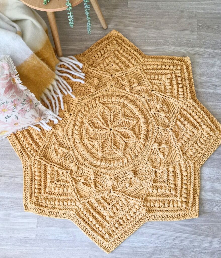 Crochet floor rug next to a table and blanket.