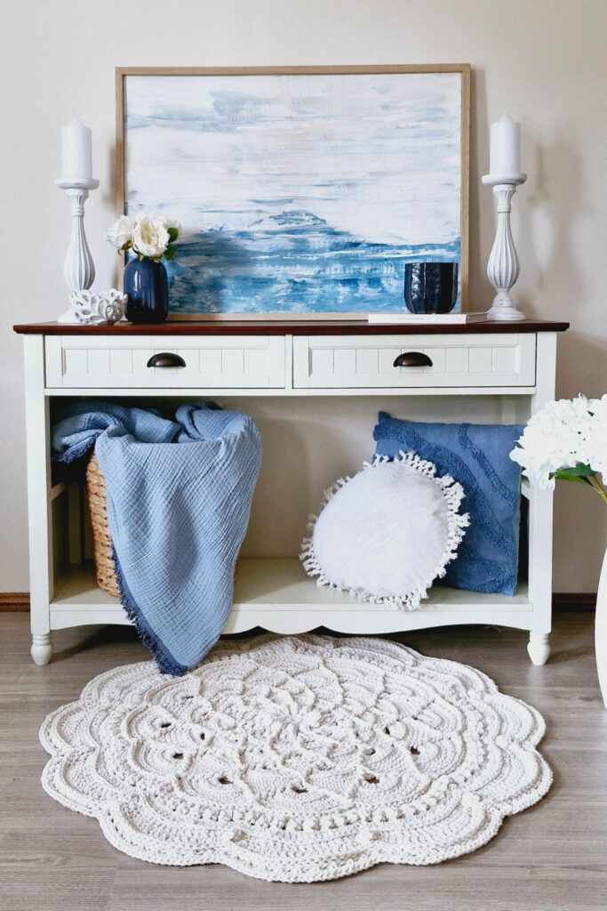 White crochet floor rug in front of a hall table decorated with Hamptons-style home decor.