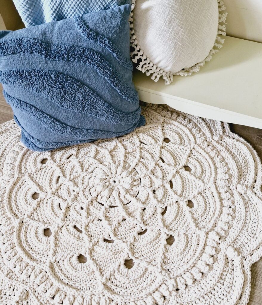 White crochet floor rug in front of blue pillow.