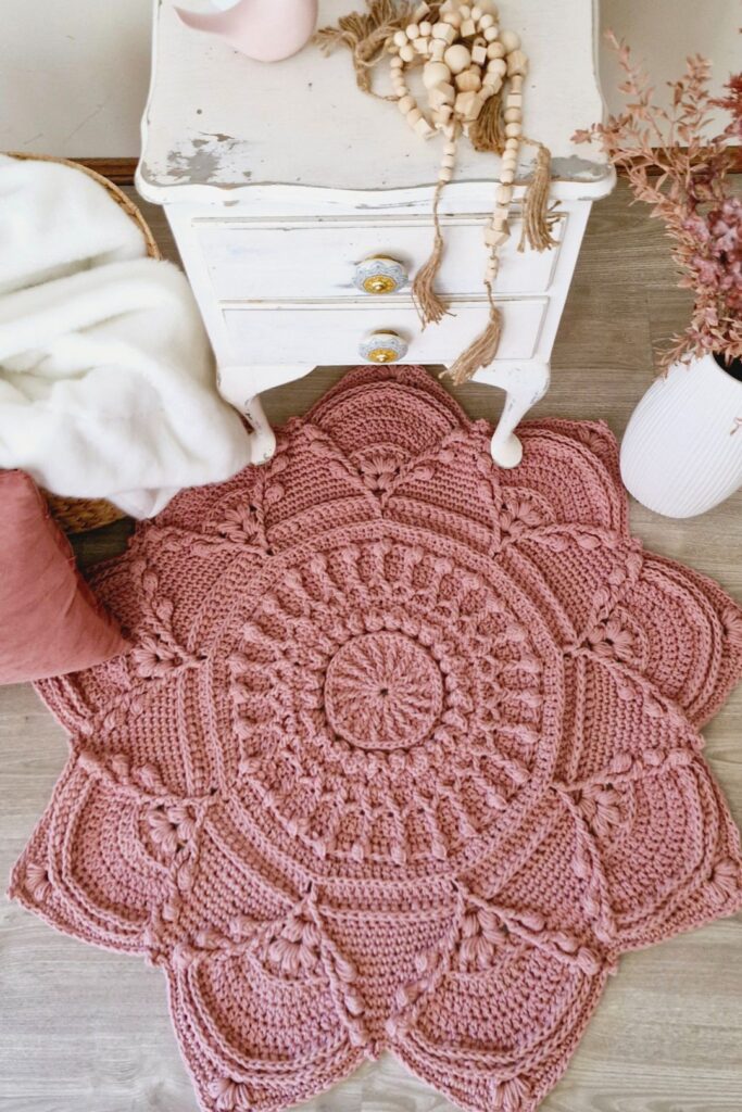 Floral crochet rug next to a white table and blankets.