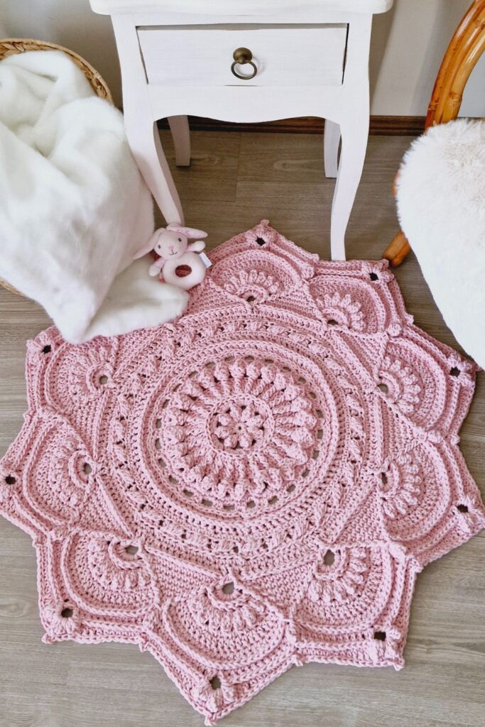 Pink crochet floor rug in front of a small table and chair.